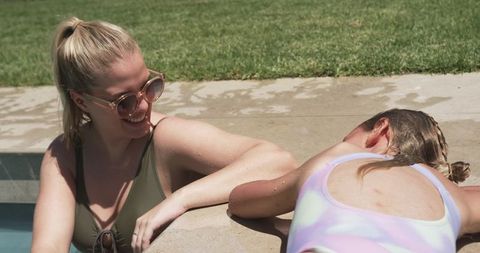 Woman and teenager relaxing and bonding poolside in backyard swimsuits on sunny day