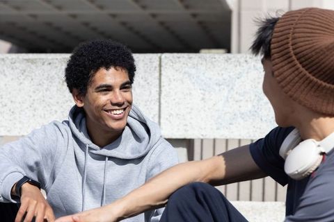 Smiling diverse teenage friends chatting on sunlit campus steps wearing hoodie and headphones