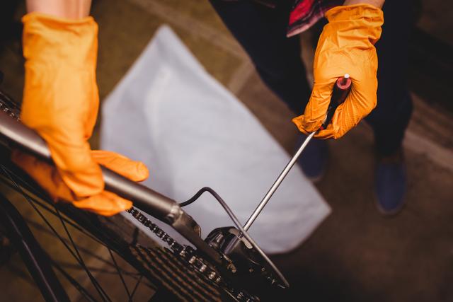 Mechanic wearing orange gloves is repairing a bicycle using tools. This photo is useful for illustrating bicycle maintenance, repair services, and DIY repair guides.