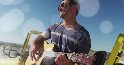 Smiling Man Playing Guitar by Beach with Lens Flares