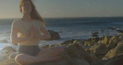 Woman meditating on rocky shore at golden hour, mindfulness and ocean serenity