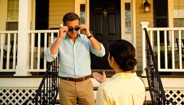 Neighborly conversation on sunlit porch by front door man adjusting sunglasses during golden hour