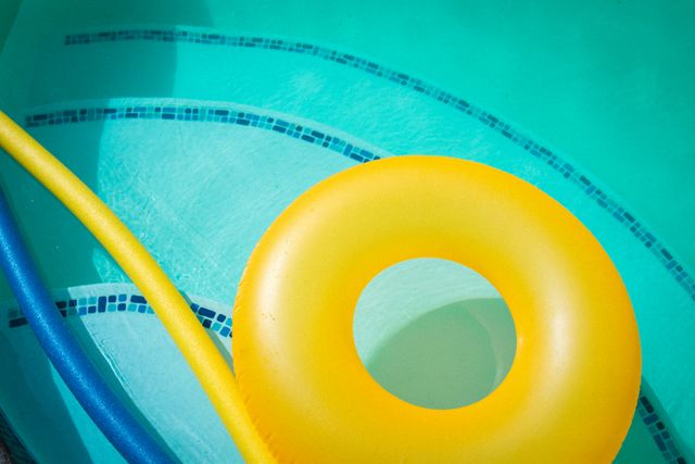 High angle view of a yellow inflatable ring and floats in a swimming pool. Ideal for use in summer vacation promotions, pool party invitations, leisure and relaxation concepts, and outdoor activity advertisements.