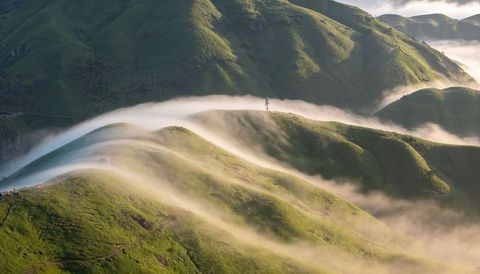Mist flowing over rolling green ridges, winding trail and antenna at sunrise