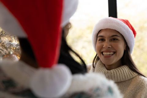 Diverse women wearing santa hats smiling, celebrating christmas together in cozy sweaters