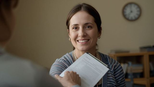 Smiling professional woman handing clipboard with form during friendly office consultation