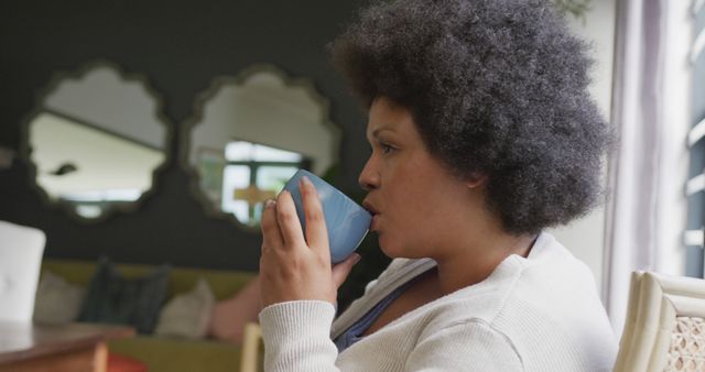 Woman enjoying a quiet moment at home, drinking coffee from blue mug. Used for promoting lifestyle, relaxation, self-care, and enjoyment of simple pleasures. Ideal for blogs, articles, advertisements, and content about daily routines.