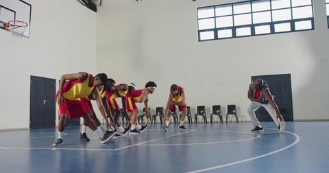Basketball Team Stretching with Coach in Indoor Gym