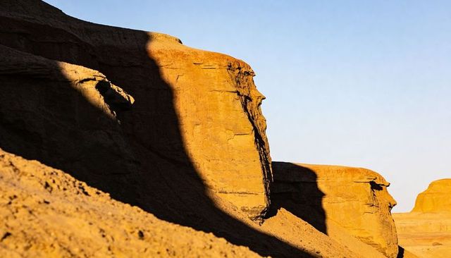 Sunlit sandstone cliffs casting long shadows over sloping talus in desert badlands dawn