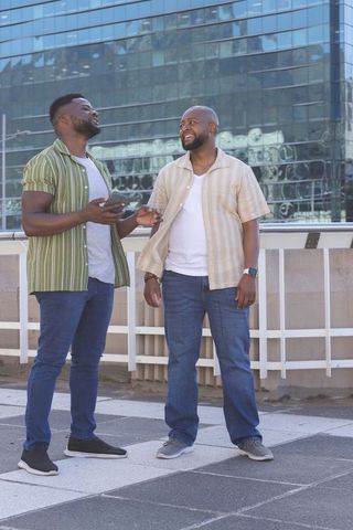 Two african american men chatting on urban rooftop with smartphone and glass reflections
