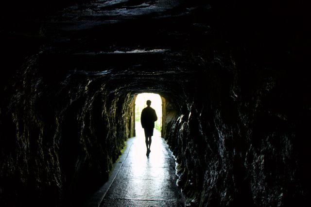 Silhouette of man walking towards light at end of dark tunnel. Captures sense of mystery, adventure, and journey. Useful for themes of exploration, escape, perseverance, and the unknown. Ideal for travel blogs, motivational content, and storytelling visuals.