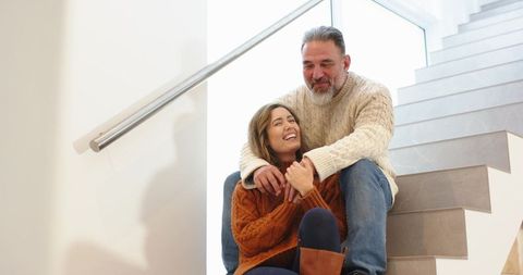 Couple sitting on staircase hugging and laughing in cozy cable-knit sweaters and boots