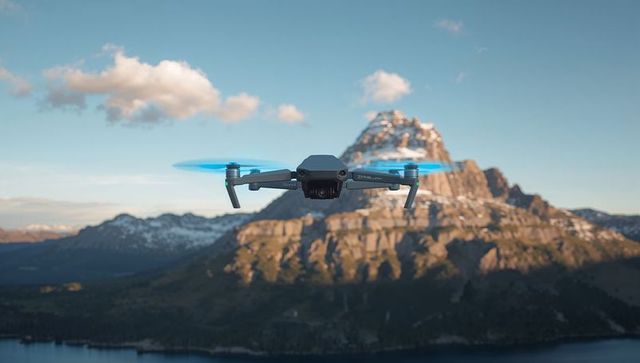 Hovering quadcopter showcasing gimbal and folding arms above alpine lake, blue prop blur