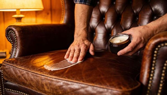 Applying leather conditioner on vintage tufted armchair seat in cozy wood-panelled den