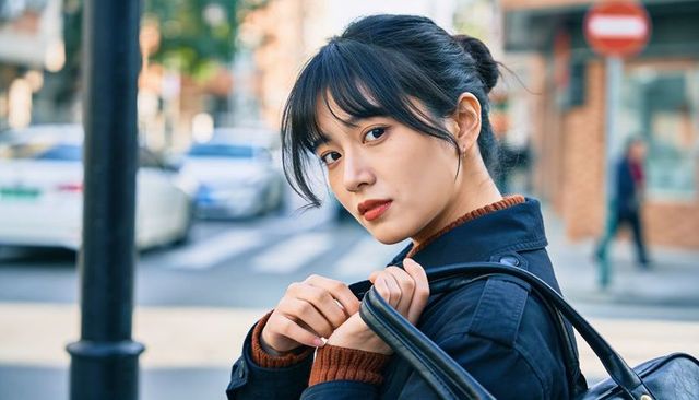 Urban candid portrait asian woman looking back holding leather bag on city sidewalk
