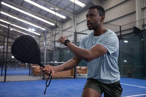 African american male swinging pickleball paddle wearing smartwatch on indoor court
