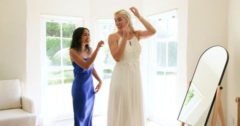 Bride with bridesmaid preparing for wedding day in bright room