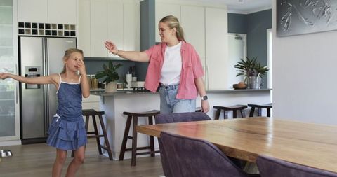 Mother guiding daughter near kitchen island while chatting in bright modern open-plan family home