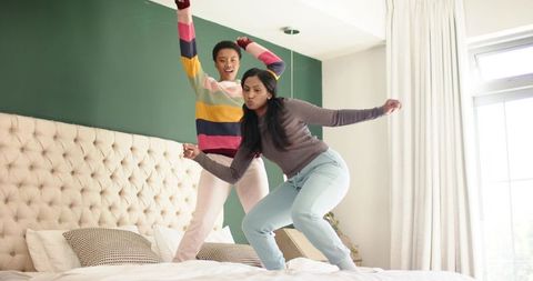 Diverse Female Friends Jumping on Bed in Cheerful Bedroom Scene