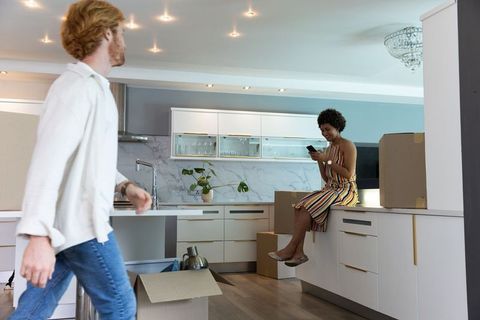 Couple Unpacking in Modern Kitchen, Woman on Counter with Smartphone