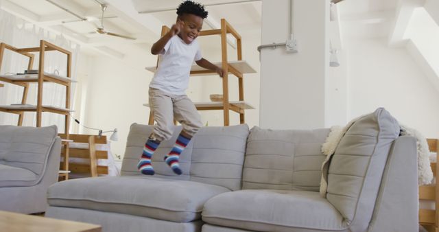 Child is energetically jumping on a couch in a modern living room, expressing joy and excitement. Great for depicting playful and active childhood moments, family life, and home furniture settings.