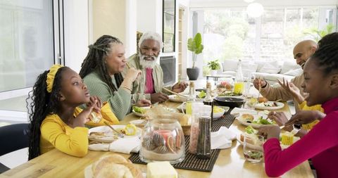 Multigenerational family sharing sunny brunch around wooden table in modern home
