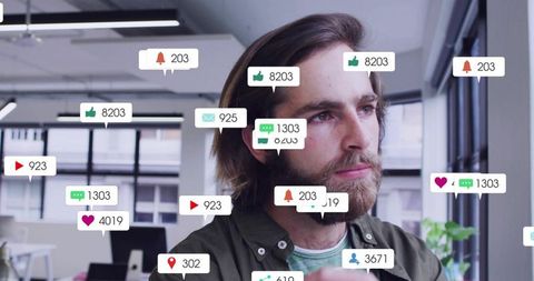 Bearded man watching screen while social notifications floating around in modern office