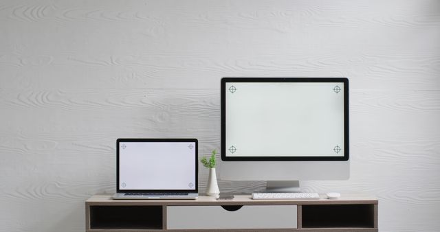 This image shows a modern home office workspace featuring a laptop and a desktop computer on a sleek wooden desk against a white background. Great for articles and blog posts about home office setups, remote work, productivity tips, and modern minimalist decor ideas.