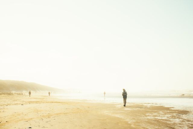 Person walking alone on misty beach during calm morning. Perfect for themes of solitude, mindfulness, tranquility, and nature. Suitable for blog posts, travel websites, meditative contexts, relaxation promotions, and peaceful environmental illustrations.