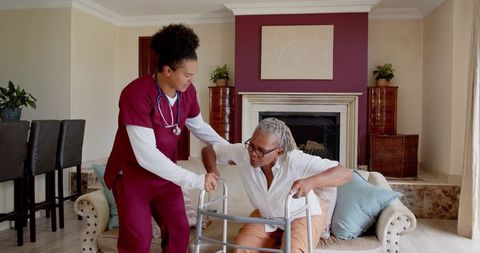 Nurse assisting elderly patient at home with walker care