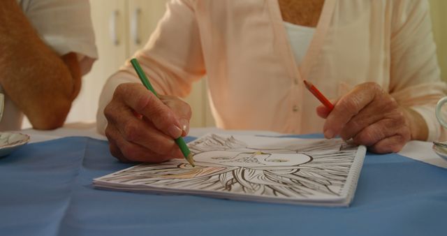 Senior woman deeply engaged in coloring with colored pencils. Hands show deliberate strokes in a coloring book. Excellent for content about healthy aging, mental wellness activities, or promoting the benefits of creativity and leisure activities for the elderly.