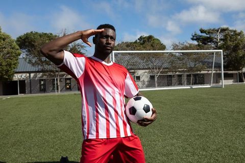 Soccer Player Posing with Ball on Field, Demonstrating Team Spirit