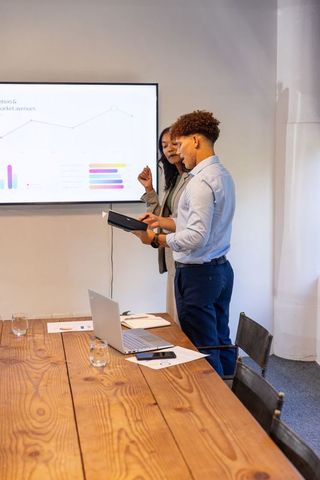 African american coworkers examining tablet referencing presentation display during meeting