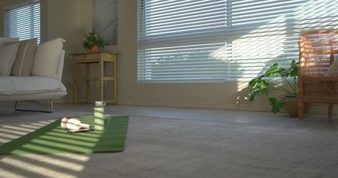 Sunlight filtering through blinds over home yoga mat with water bottle and headphones