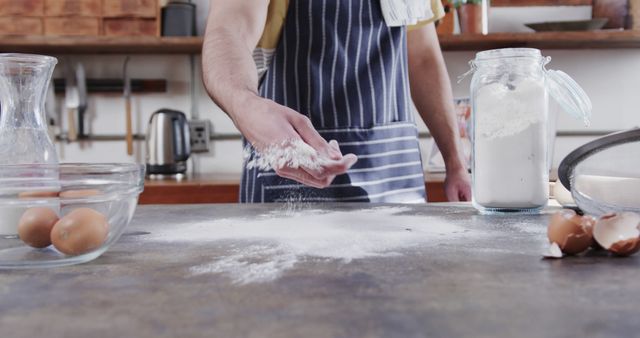 Person preparing to bake, sprinkling flour on kitchen counter. Ideal for articles, blogs, or websites related to baking, cooking, home kitchens, and culinary arts. Can be used for promotional material for baking classes, flour, or other baking ingredients.