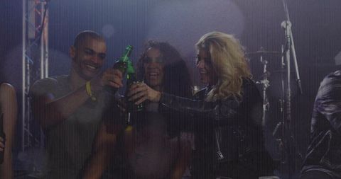 Friends Toasting with Green Beer Bottles on Club Stage at Live Concert Celebrating Nightlife
