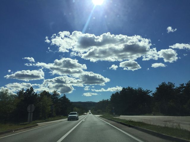 Perfect for use in travel brochures, driving safety campaigns, advertisements for road trips, wallpapers, or articles relating to serene journeys or road conditions. The bright blue sky with fluffy clouds exudes a sense of clarity and peaceful driving on an open road.