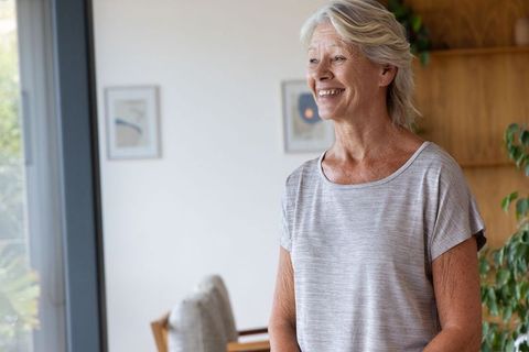 Smiling senior woman standing by floor-to-ceiling glass door in bright modern home interior