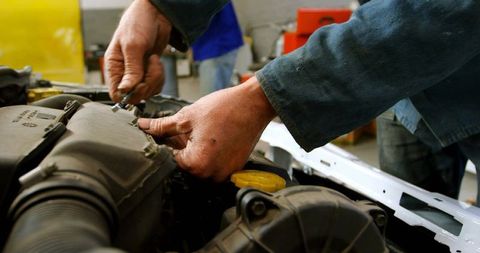 Mechanic tightening intake hose bolts on car engine with yellow oil cap, garage