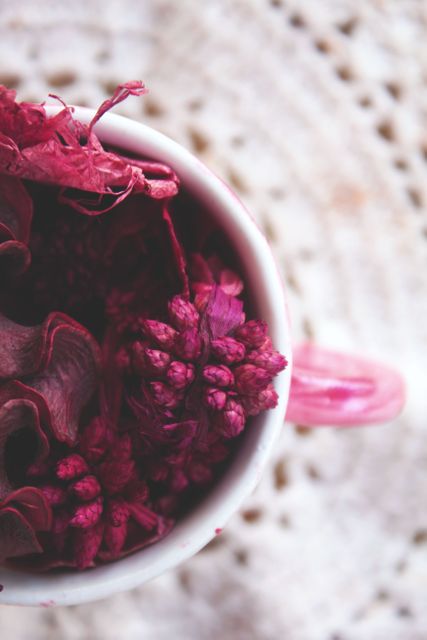 This calming close-up of pink potpourri in a ceramic cup, juxtaposed with a crocheted background, exudes a warm and cozy feel. Perfect for blogs about home decor, DIY projects, and craft tutorials, the image highlights delicate details, appealing to audiences interested in aesthetic home embellishments.