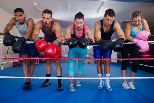 Group of young boxers taking a break during an intense training session in a boxing ring. Ideal for use in fitness and sports-related content, promoting teamwork, determination, and the physical demands of boxing. Suitable for articles, advertisements, and social media posts about athletic training, boxing, and gym workouts.