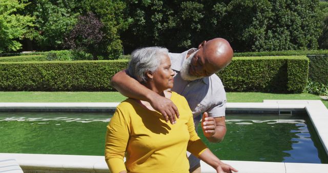 Mature couple sharing a warm moment near pool. They are lovingly interacting against a lush green backdrop. This can be used for themes related to older couples, love and affection, outdoor leisure, retirement lifestyle, and summer relaxation visuals.