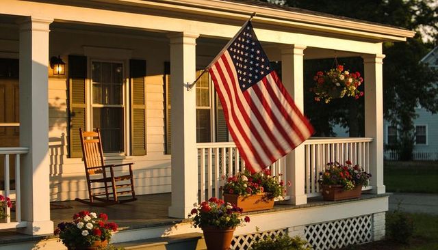 Waving american flag on sunny front porch with rocking chair and colorful flower pots