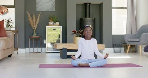 Teenage girl meditating on yoga mat in minimalist living room for mindfulness and calm