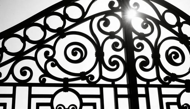 Backlit ornate wrought-iron gate featuring spiral scrolls, arch symmetry and sun starburst