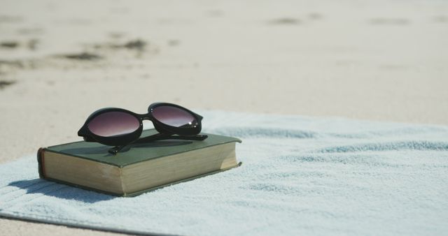 Sunglasses and book on beach towel at sunny beach, copy space. Vacations, summer, free time and relaxation.