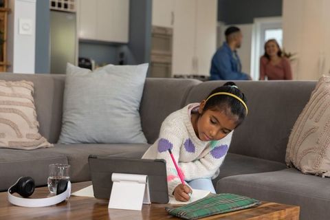 Girl studying on sofa with tablet and notebook in modern open-plan living room for home learning