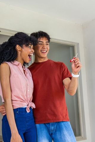 Diverse young couple celebrating first home with red key fob showing joy and pride