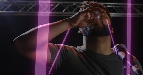 Male performer drinking shot onstage while raising arm toward mic neon pink light streaks
