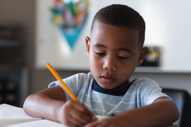 Serious african american elementary schoolboy writing on book at desk in classroom. unaltered, education, studying, learning, concentration and school concept.